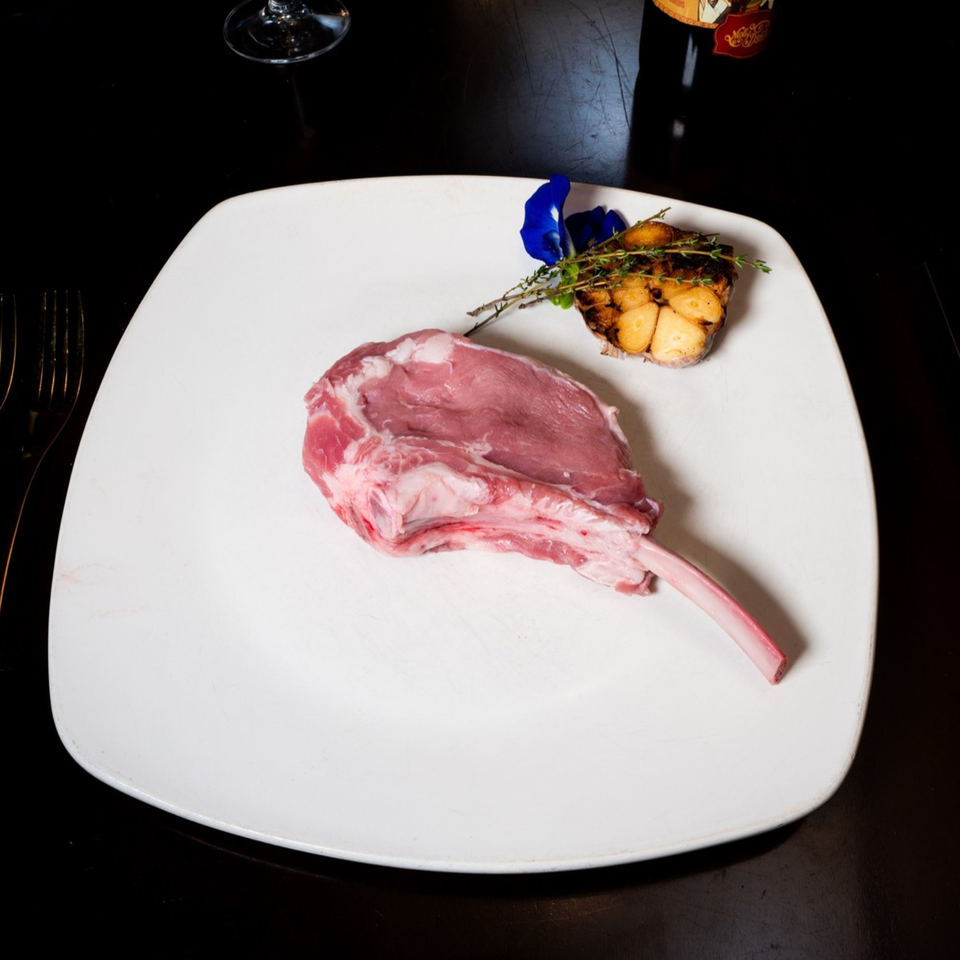 A raw Tomahawk steak with roasted garlic and herbs on a white plate at Polo Steak and Sea.