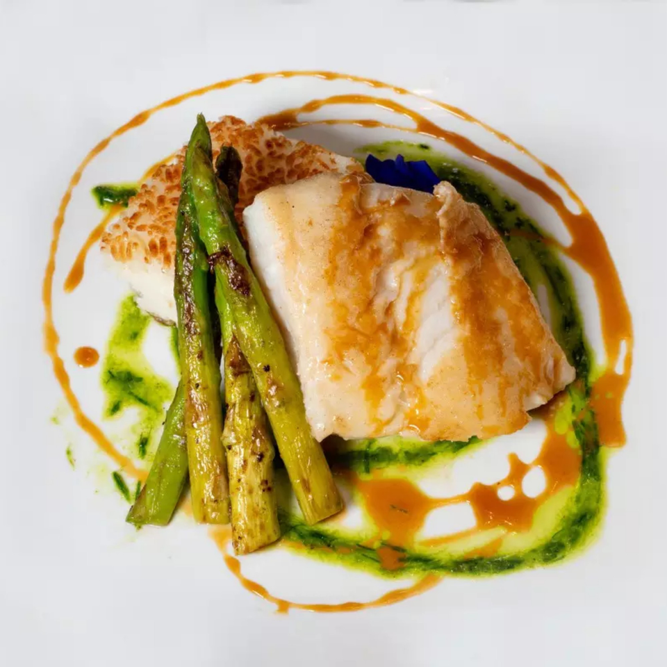 Pan-seared sea bass with grilled asparagus, crispy rice, and vibrant sauces on a white plate.