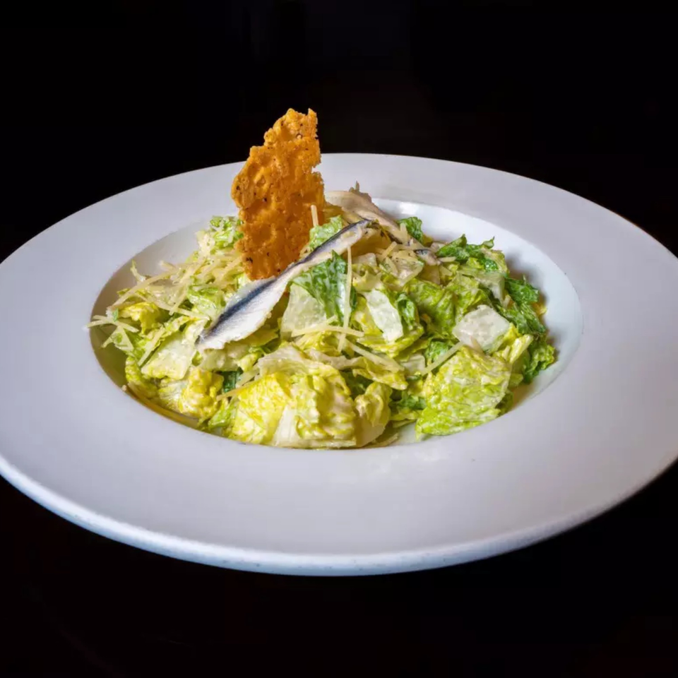 Caesar salad with anchovies, parmesan, and a large cheese crisp on a white plate.